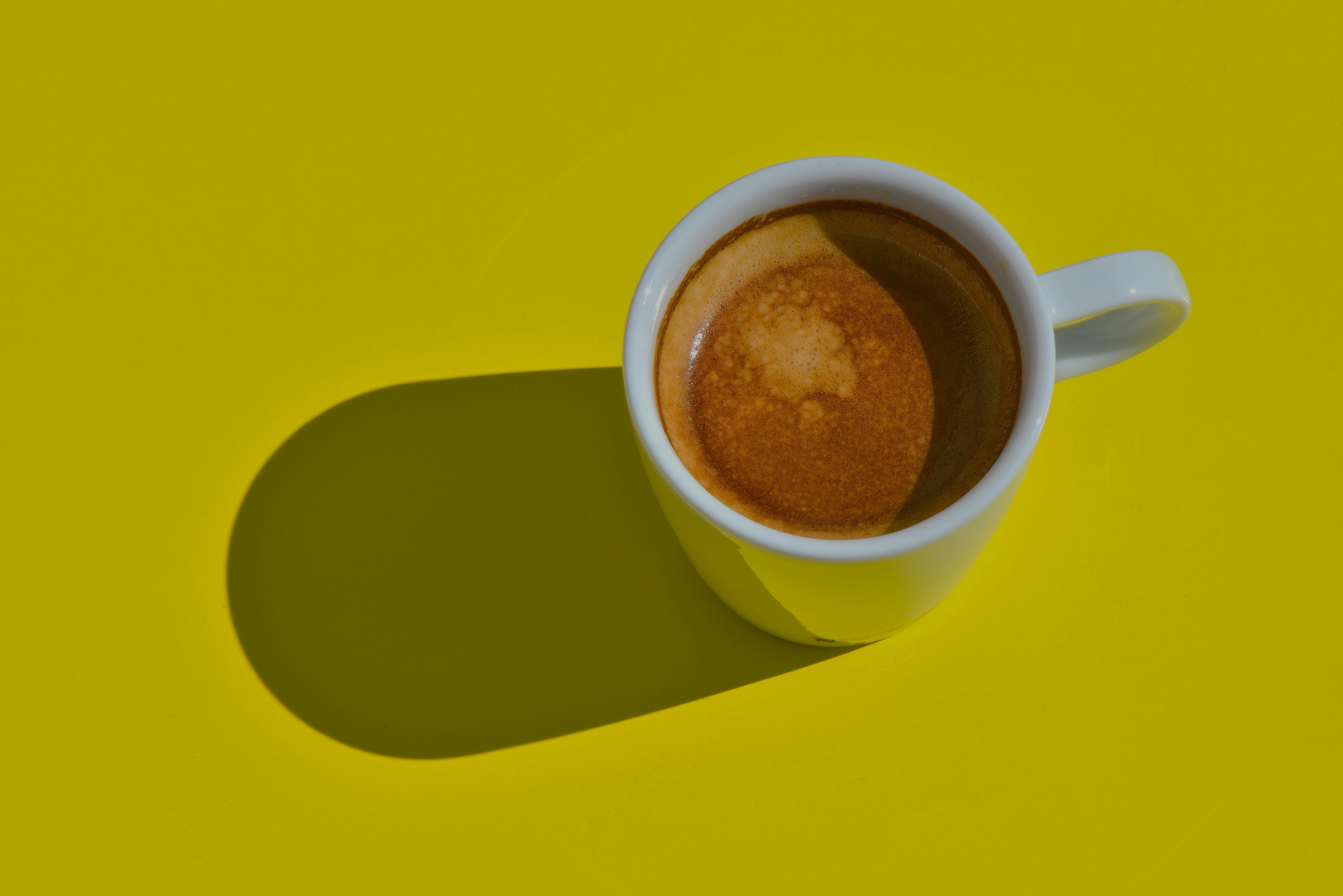 A cup of coffee sits on a yellow background
